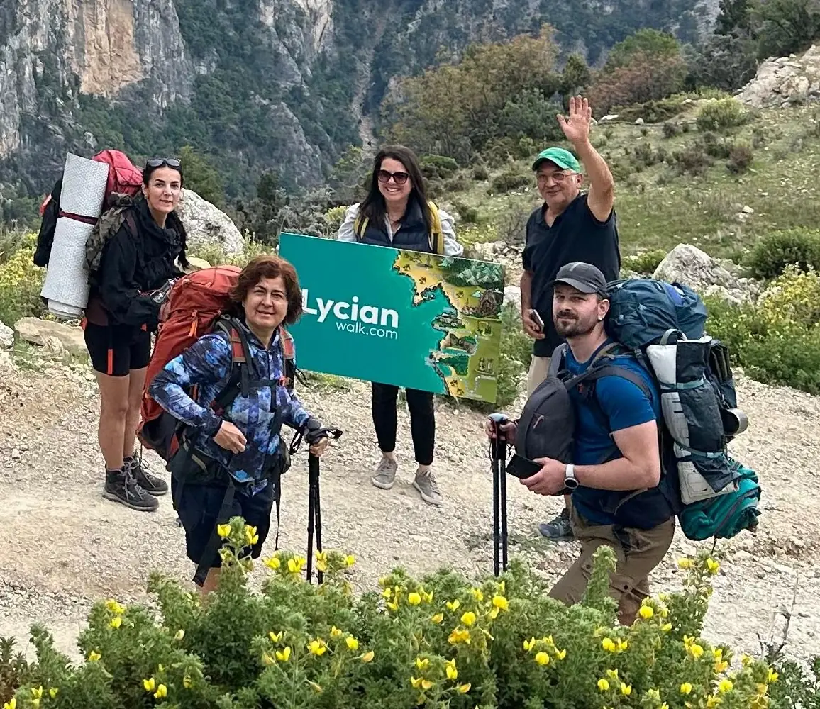 Guided hiking group on the Lycian Way holding a LycianWalk.com route map board on a mountain trail in southwest Turkey.