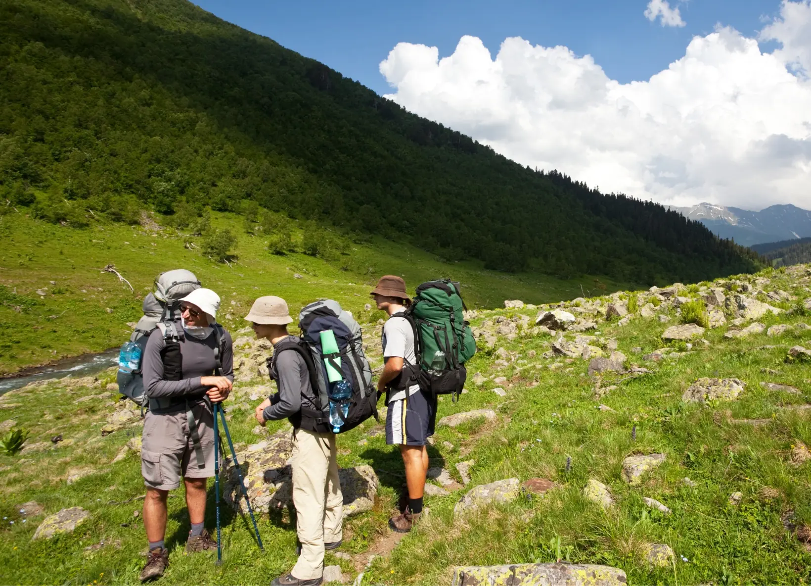 Backpackers Hiking Through the Lycian Way Mountain Valley Group of backpackers walking across a scenic mountain valley on the Lycian Way, surrounded by lush green hills and dramatic cloud formations.