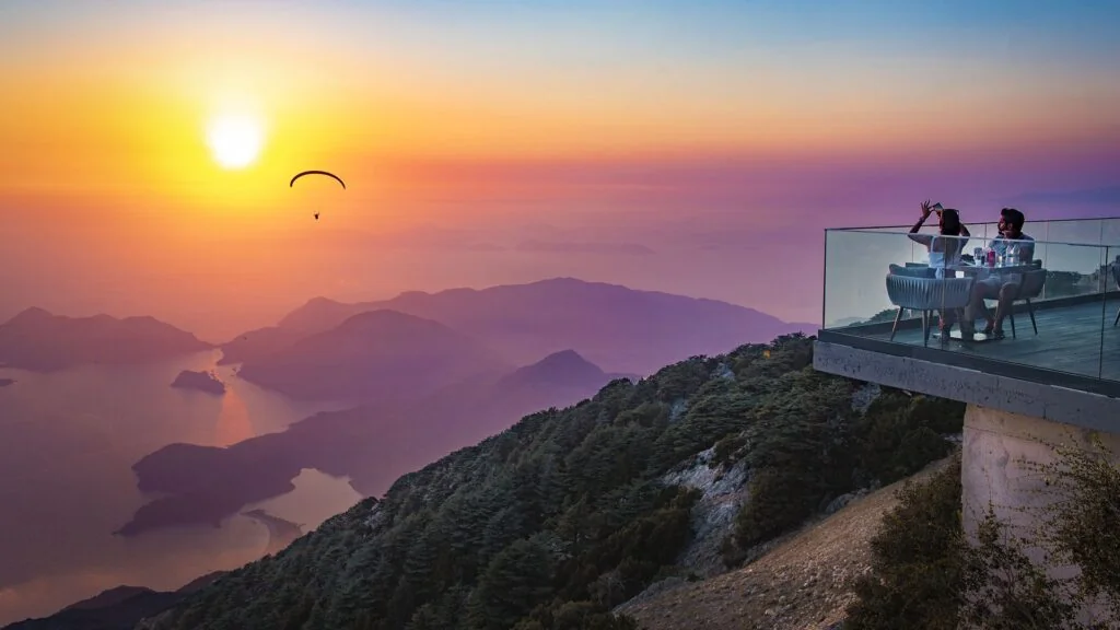 Sunset panorama from Babadağ above Ölüdeniz featuring paragliding over the Blue Lagoon and Mediterranean coastline in the Lycian Way region of Turkey.