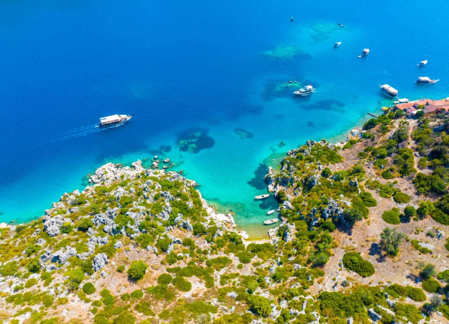 Aerial view of a turquoise bay along the Lycian Coast in Turkey with rocky shoreline, clear Mediterranean water and anchored boats near the hiking routes of the Lycian Way.