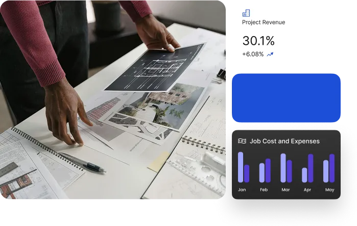 A person is reviewing architectural plans and financial data on a white table. The plans include blueprints and renderings of buildings. The financial data includes a graph of job costs and expenses, and a report of project revenue.