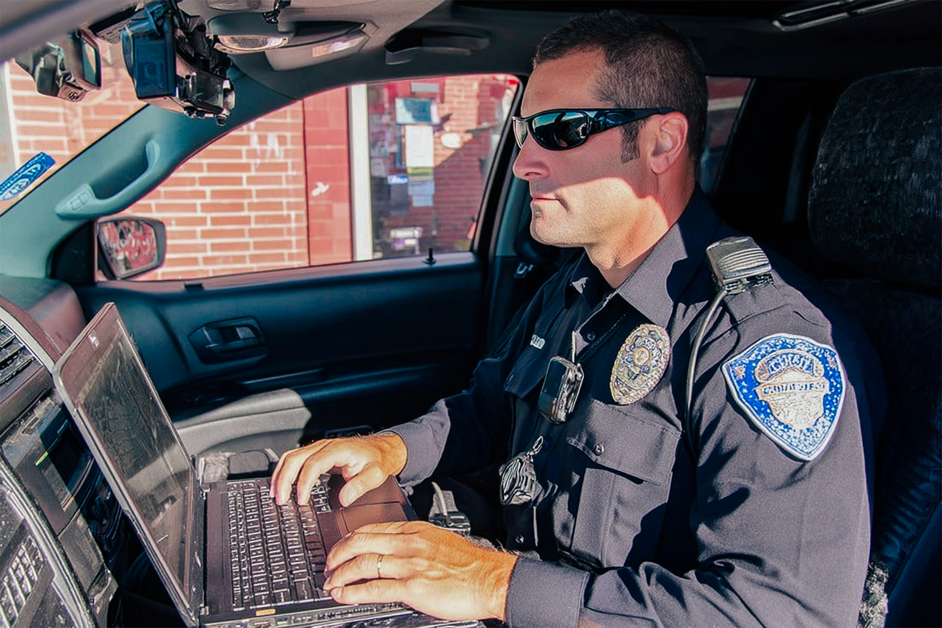 A police officer typing into his laptop while parked in a police cruiser
