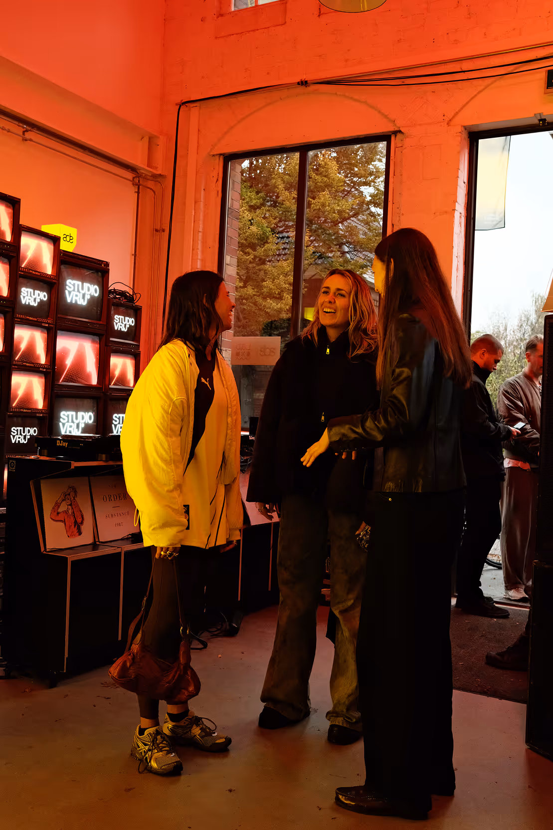 Studio Vrij team member introducing VR Silent Disco experience to arriving participants in red-lit onboarding area during ADE premiere, with Studio Vrij branding visible.