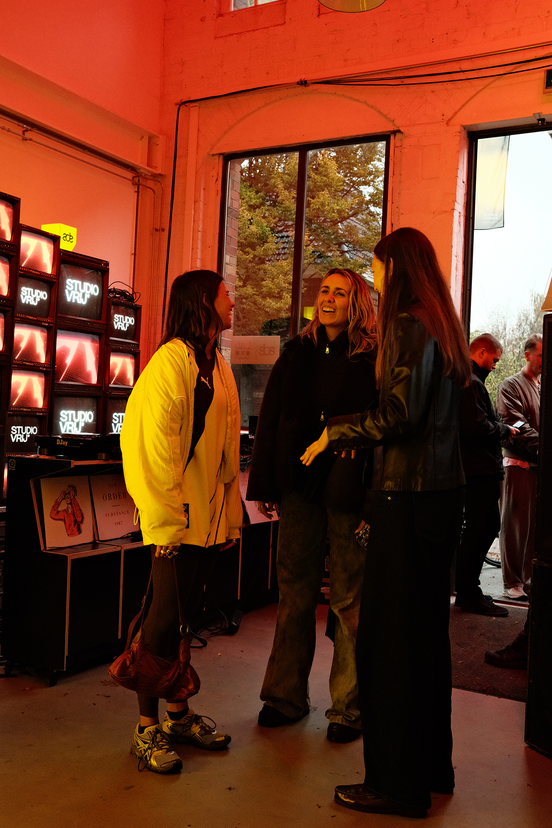 Studio Vrij team member introducing VR Silent Disco experience to arriving participants in red-lit onboarding area during ADE premiere, with Studio Vrij branding visible.