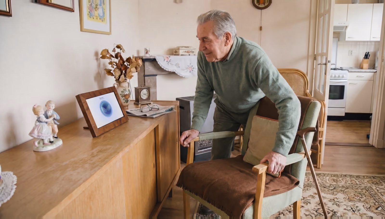 Oudere man bij zijn dressoir, op het punt een gesprek te beginnen met Zuster Annie op de tablet