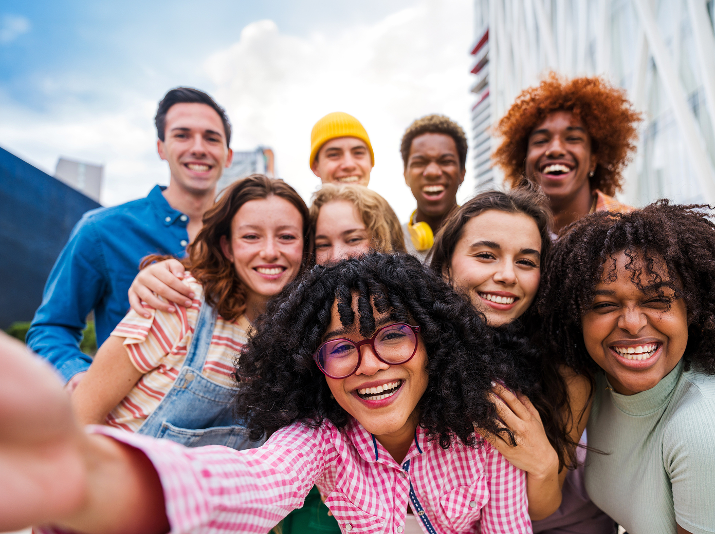 Group of diverse young adults smiling closely together taking a selfie outdoors.