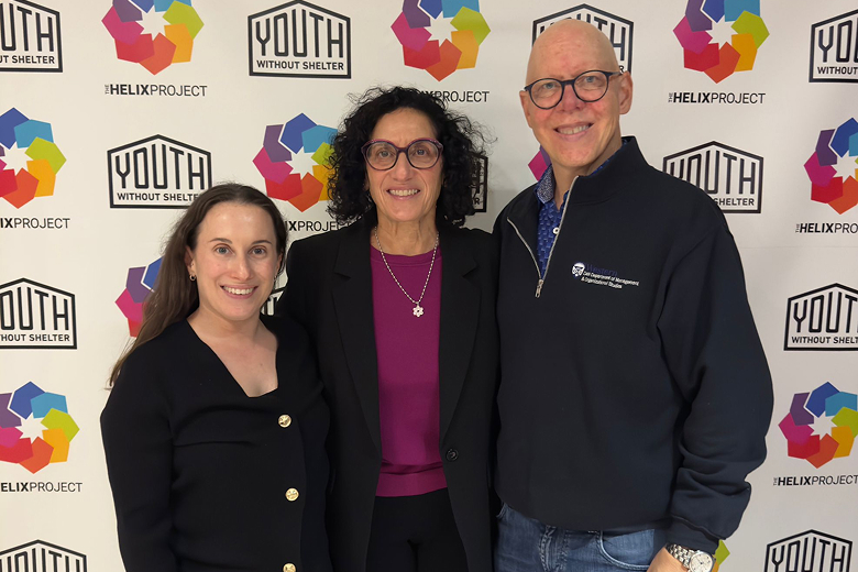 Three adults smiling in front of a backdrop with Youth Without Shelter and The Helix Project logos.