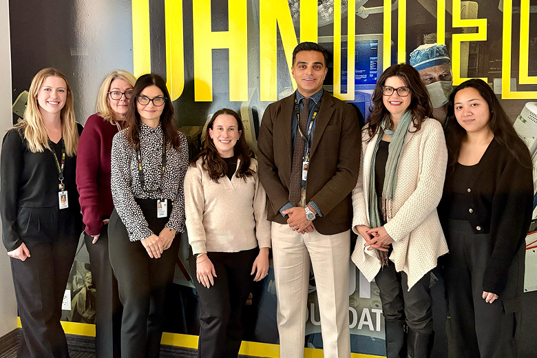 Group of seven professional individuals standing indoors in front of a wall with large yellow letters.