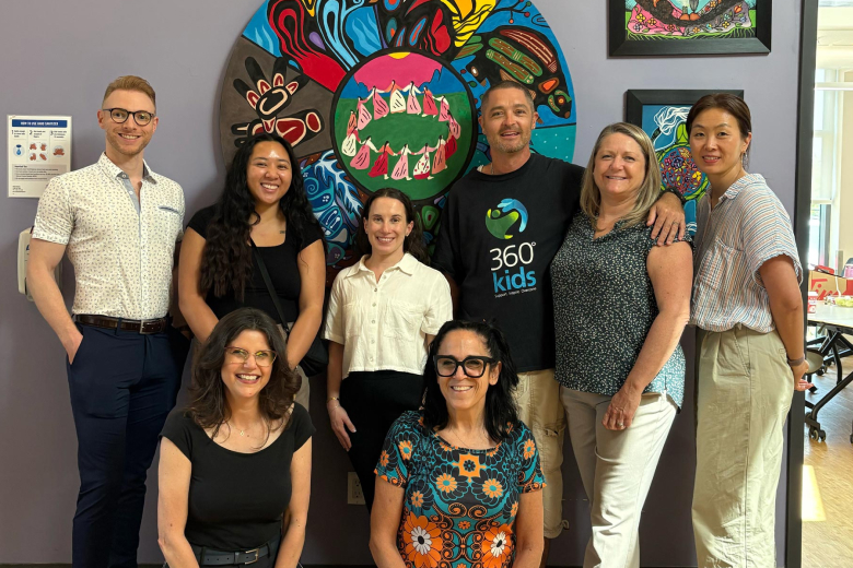 Group of eight diverse adults smiling and posing in front of colorful circular and framed wall art in a bright room.