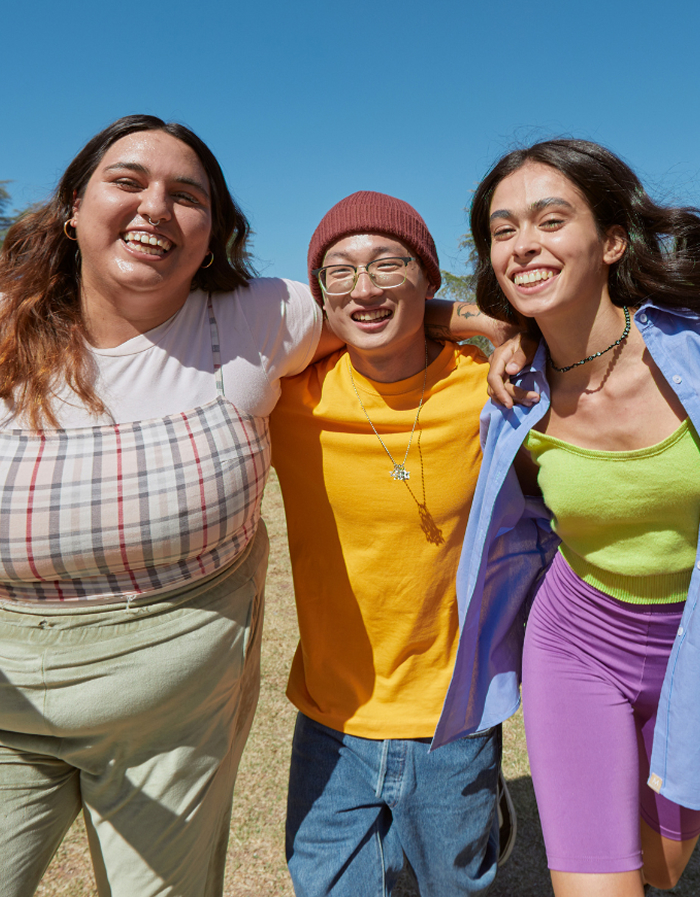 Three friends smiling outdoors with their arms around each other under a clear blue sky.