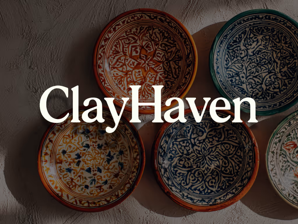 Roofer in safety harness kneeling on a sloped residential roof, preparing shingles against a backdrop of houses and tree-lined streets.
