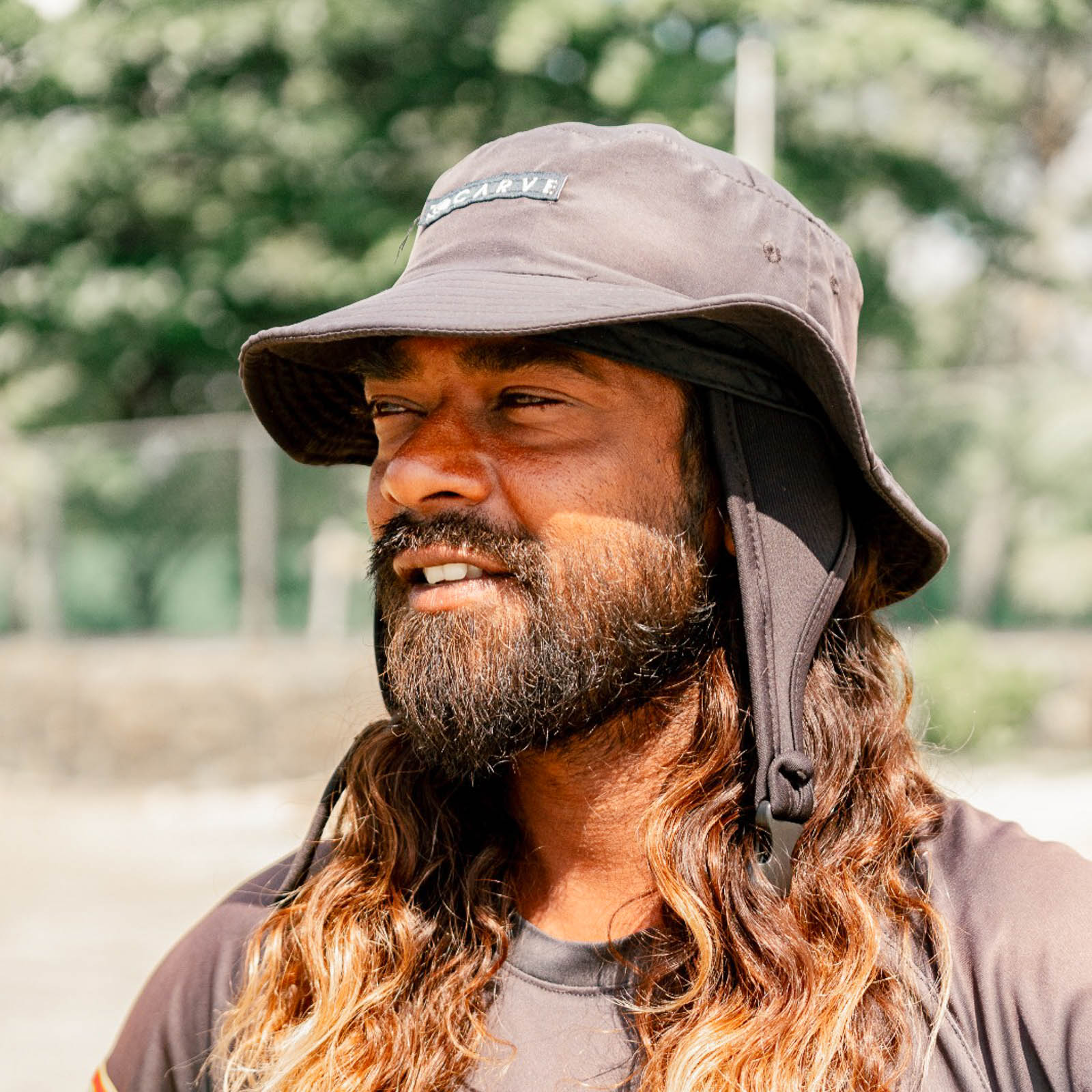 Surf coach Loku from Beach Love Surf School in Galle, Sri Lanka, smiling under his sun hat at the beach.