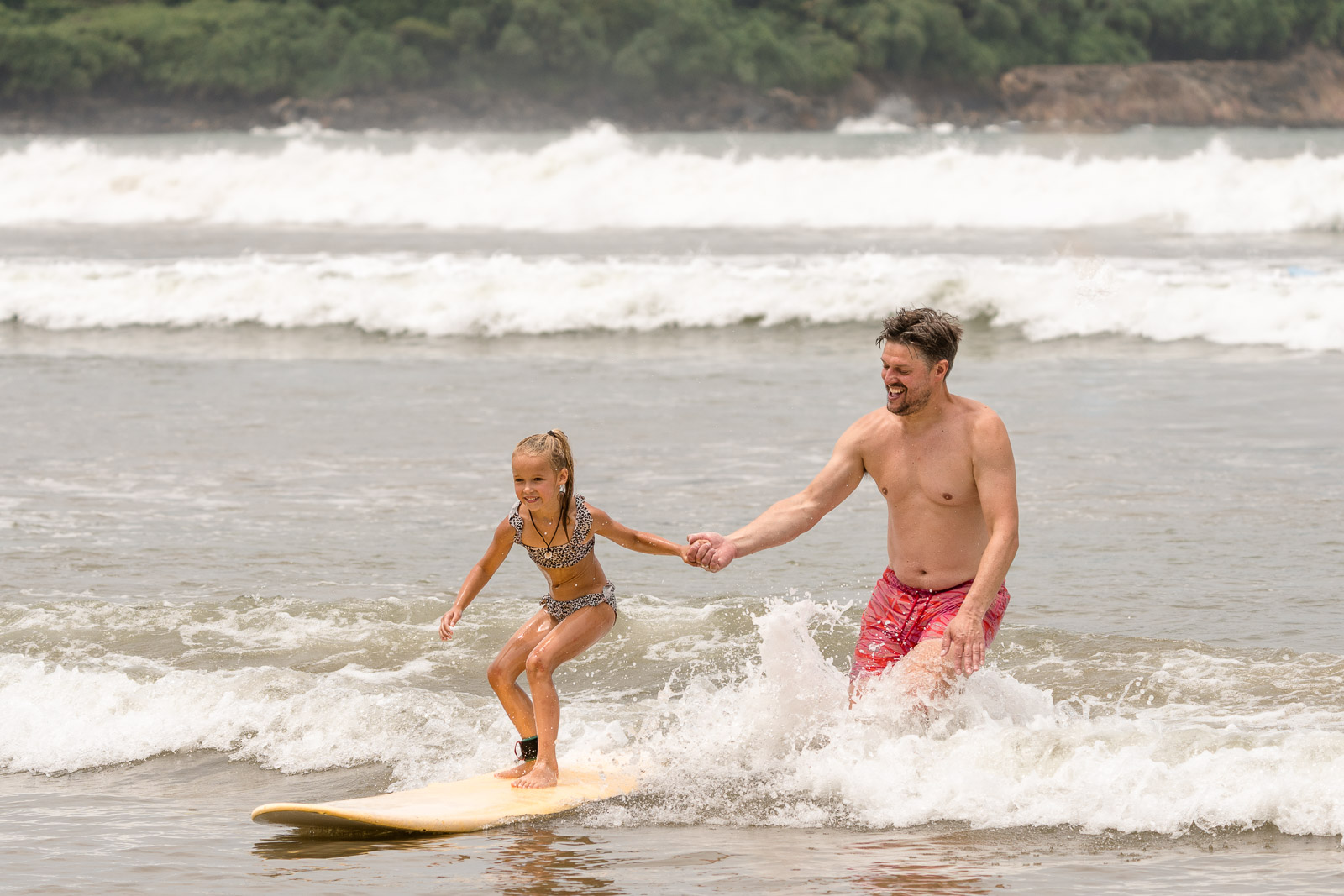 Father helping his daughter catch her first wave during a family surf lesson at Dewata Beach, Galle, Sri Lanka.