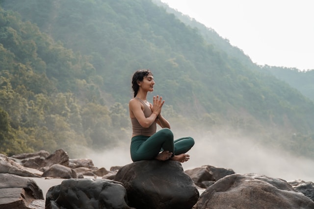 Woman practicing yoga and meditation on rocks surrounded by mist and jungle mountains in Sri Lanka.