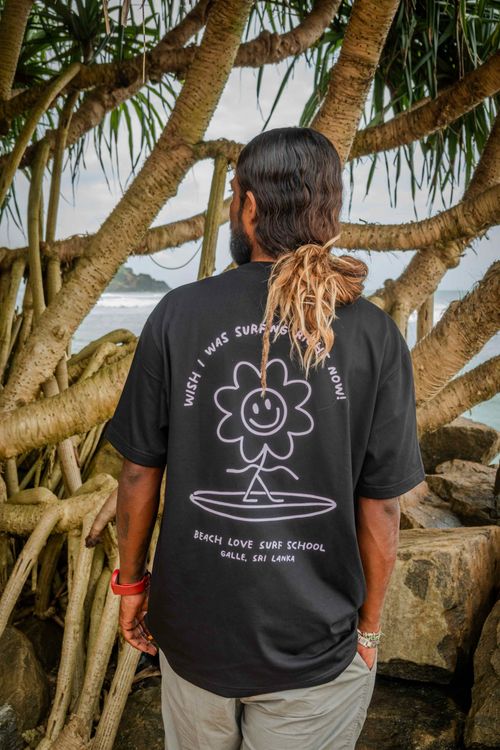 Surf coach wearing a Beach Love Surf School t-shirt with a smiley flower surf design at the beach in Galle, Sri Lanka.