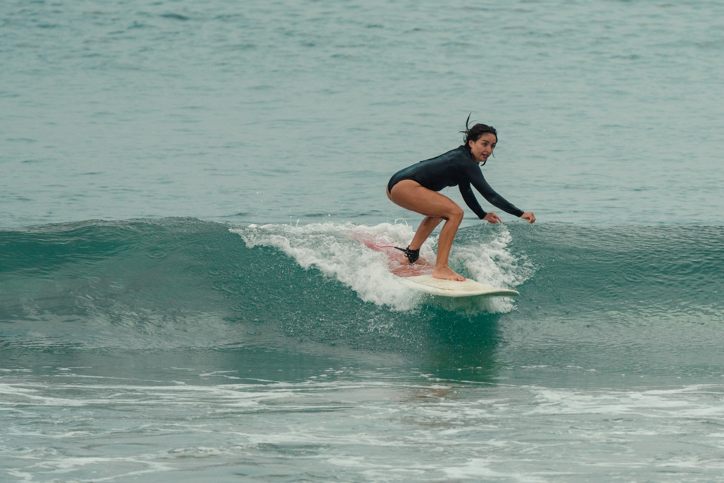 Female surfer riding a small clean wave during a surf lesson with Beach Love Surf School at Dewata Beach, Galle, Sri Lanka.