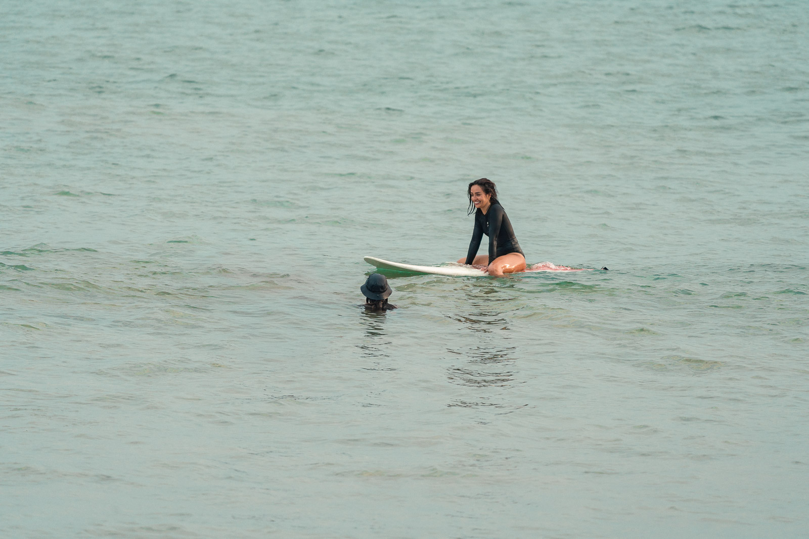 Surf student smiling on a surfboard during a lesson with her instructor in the water at Dewata Beach, Galle, Sri Lanka.
