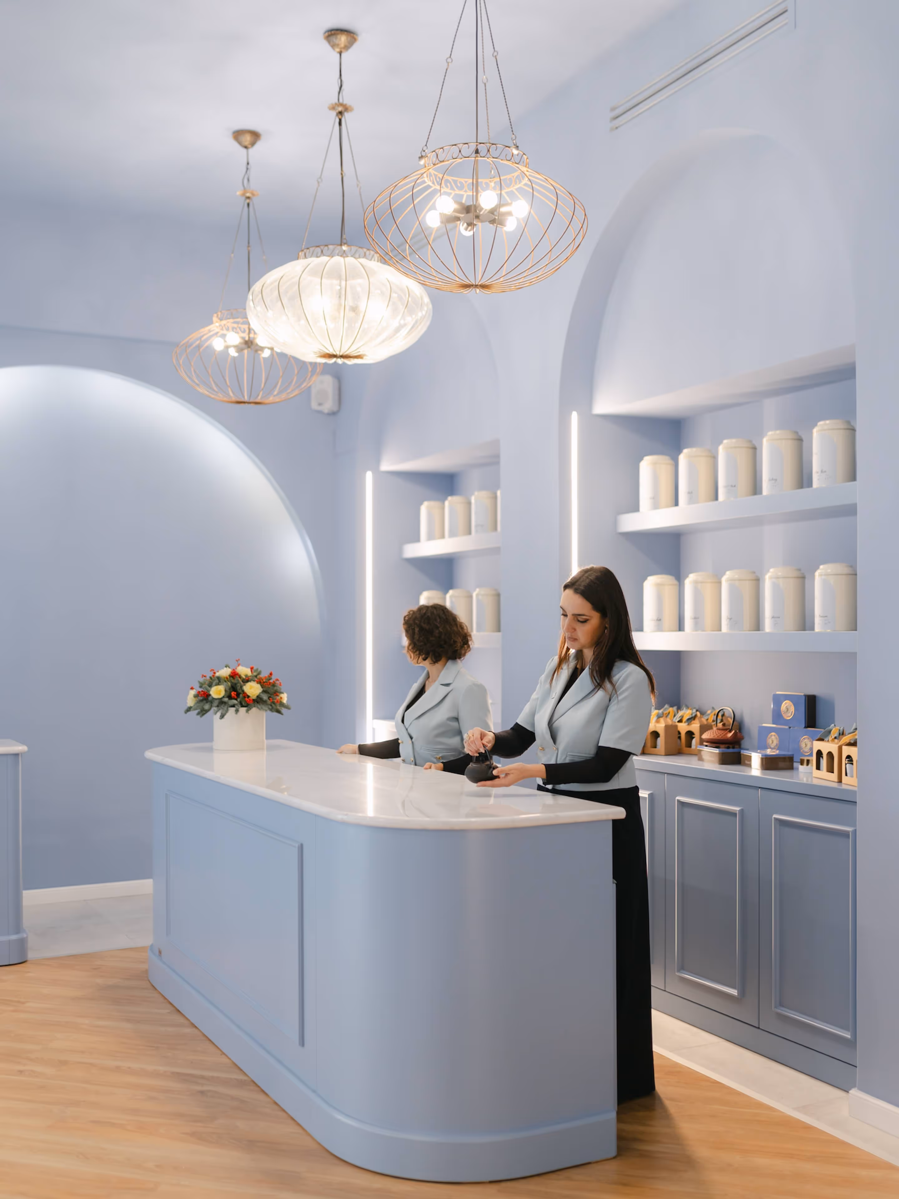 Interno di un'elegante sala da tè con pareti azzurre ornate da archi, lampadari e un bancone in marmo dietro il quale ci sono due donne in uniforme.