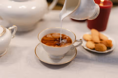 Versamento di latte in una tazza di tè nero, con biscotti al burro.
