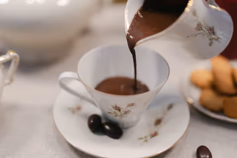 Versamento di cioccolata calda in una tazza da tè bianca, con biscotti al burro.