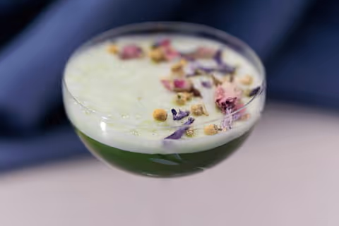 Cocktail al tè matcha in bicchiere con schiuma bianca e guarnizione di floreale.