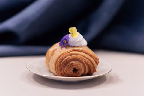 Viennoiserie lievitata e arrotolata, decorata con crema e un fiorellino viola.