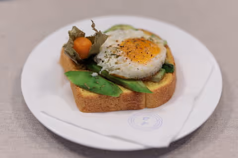 Toast con uovo all'occhio di bue e verdure, su piatto bianco.