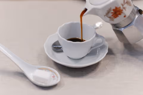 Versamento di caffè in una tazza da espresso con zolletta di zucchero su piattino.