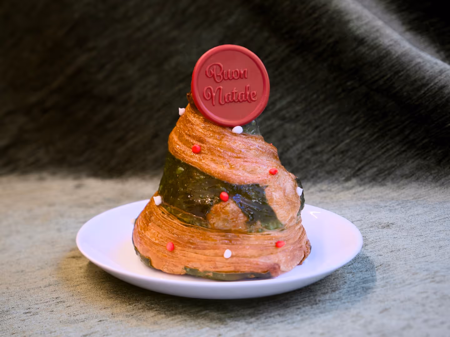 Croissant a forma di albero di Natale, decorato con crema e confetti rossi e bianchi, con un sigillo "Buon Natale".