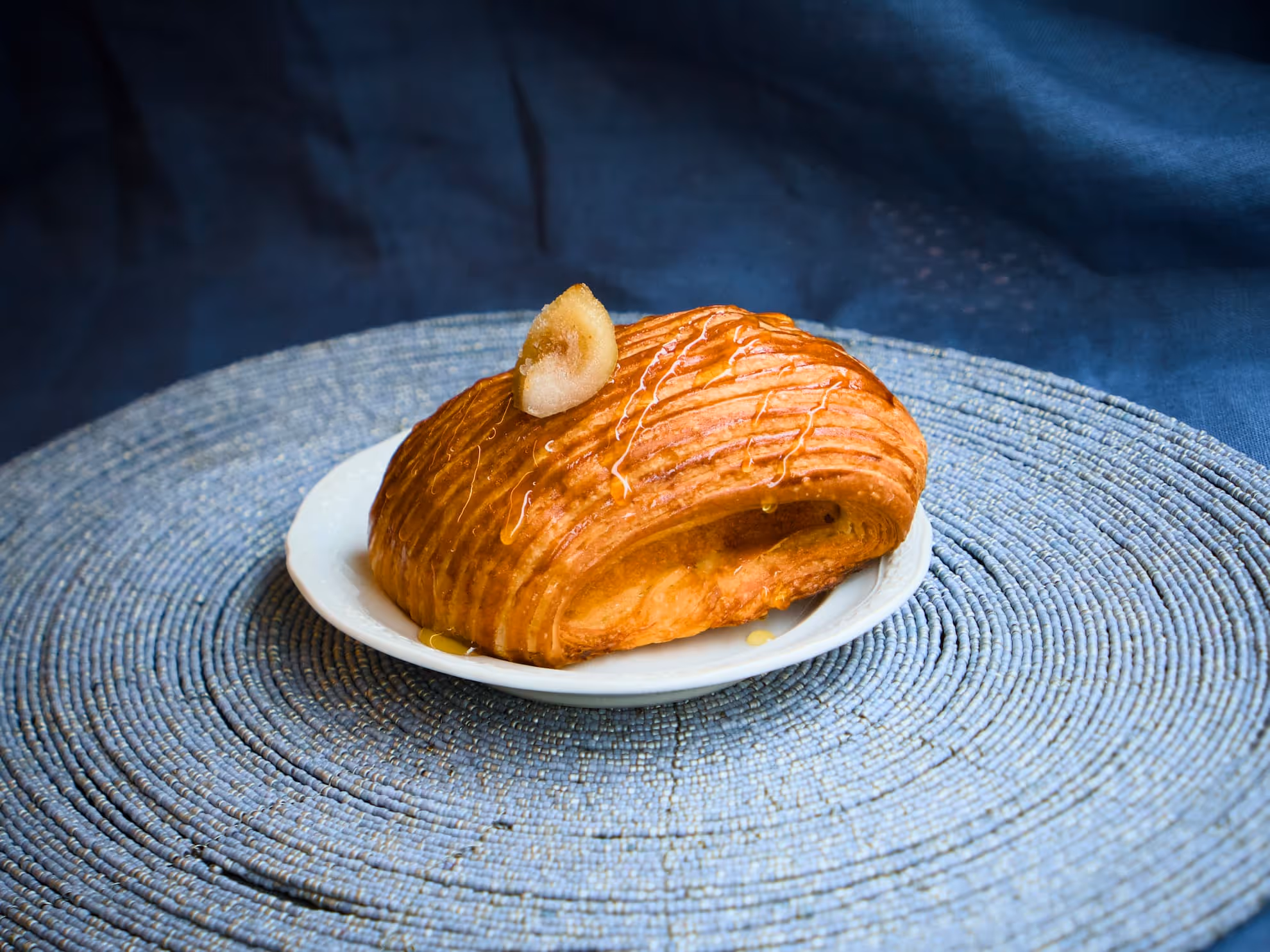 Viennoiserie dorata ricoperta di miele e guarnito con fichi, servito su un piattino bianco.