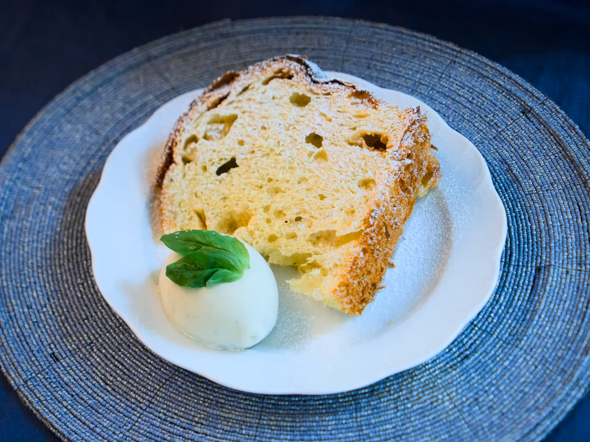Fetta di panettone spolverata di zucchero a velo accanto a una quenelle di gelato al limone con foglia di basilico.