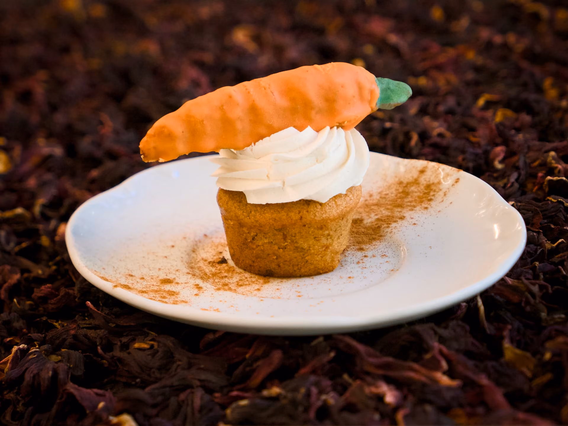 Carrot cake con crema al burro e carota di marzapane, su piattino bianco spolverato di cannella.