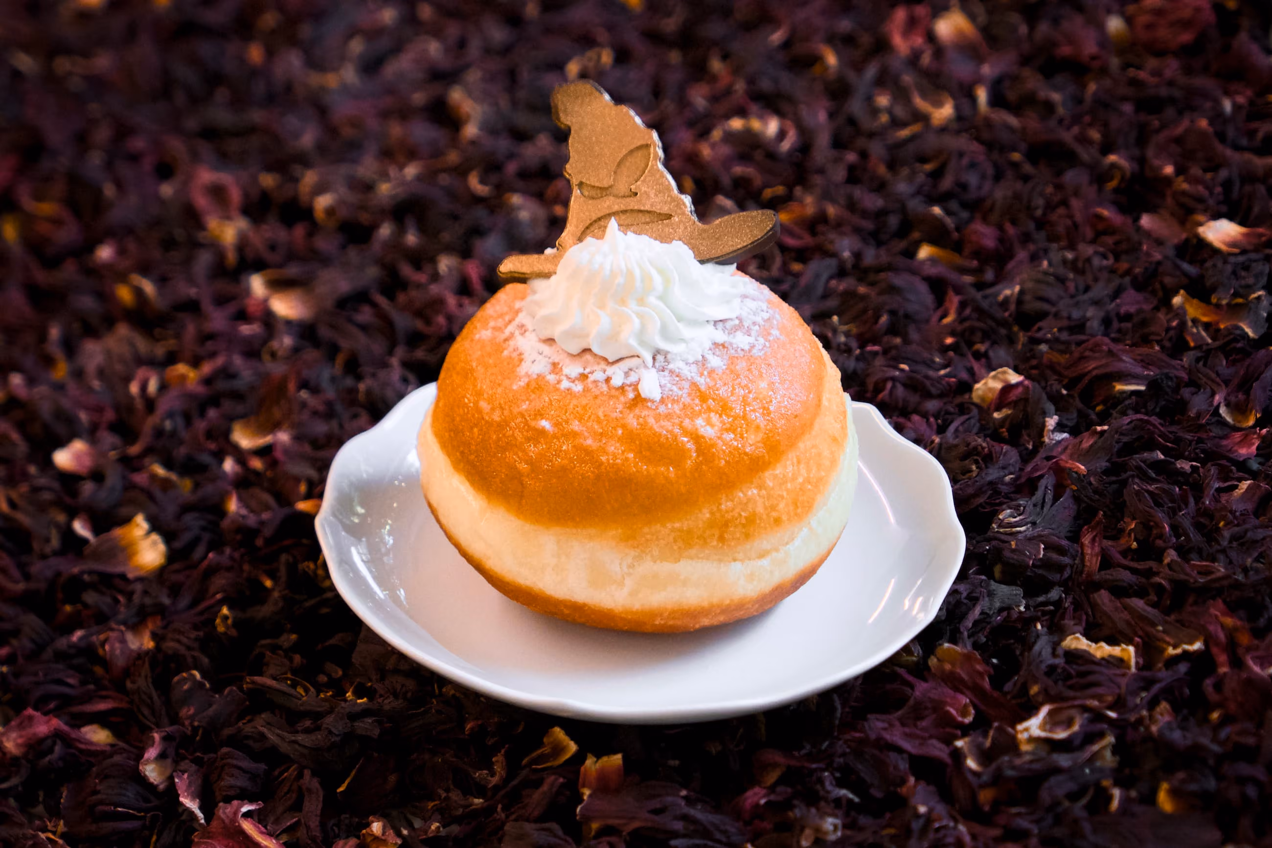 Krapfen spolverato di zucchero a velo, con un ciuffo di panna e una decorazione dorata a forma di cappello da mago.