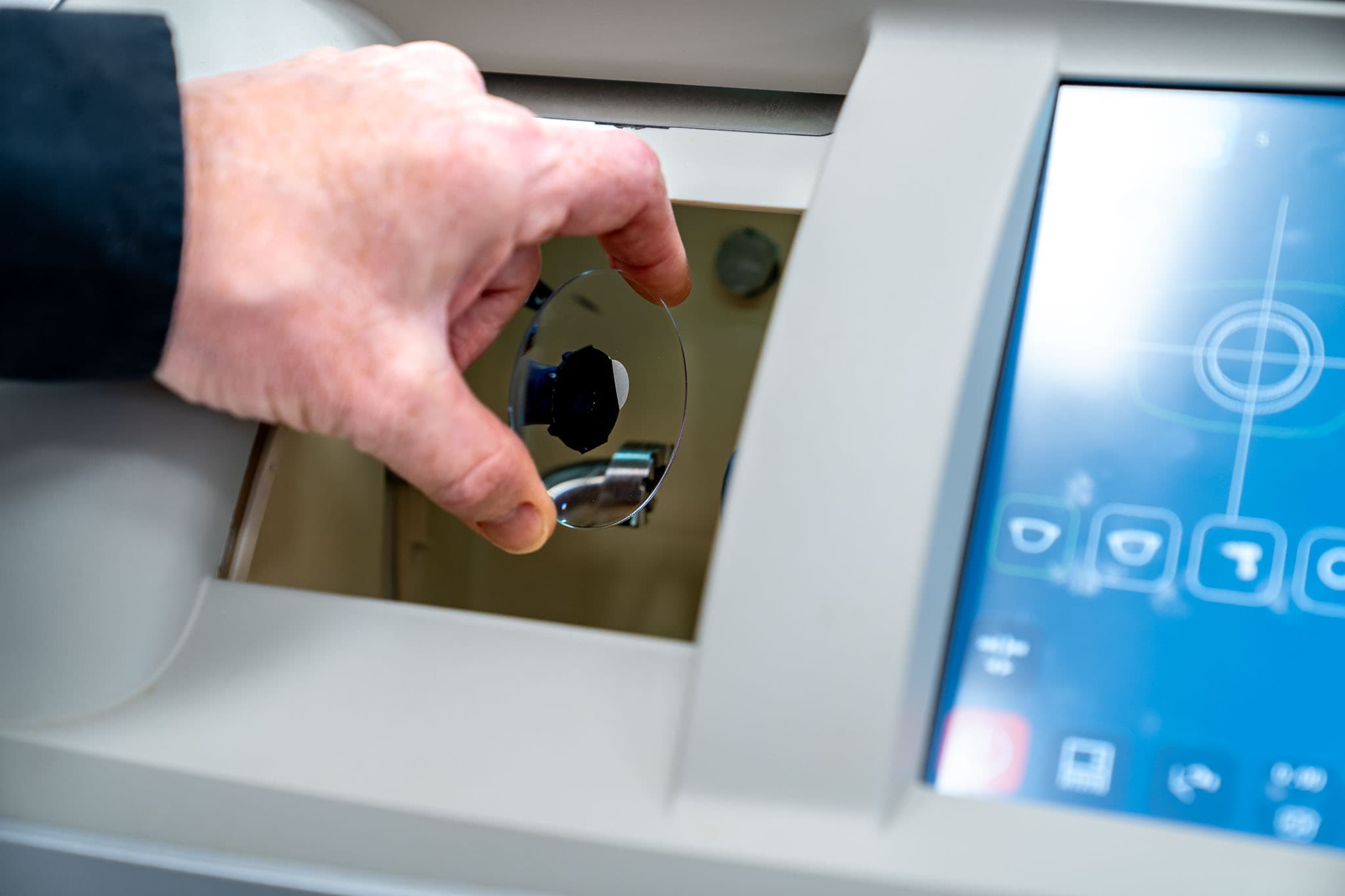 Eine Hand, die ein Brillenglas zur Brillenherstellung in ein Gerät legt