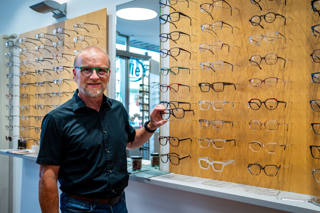 Optiker präsentiert Brillenfassungen vor einer großen Auswahl im Laden Die Brille Dömer.