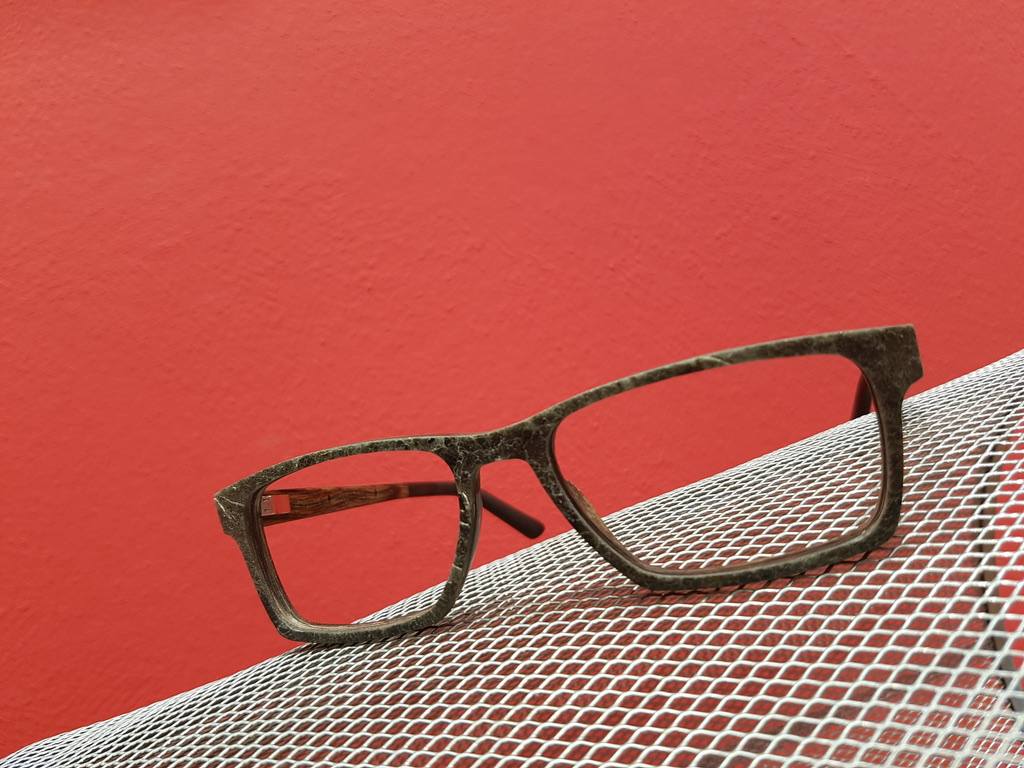 Brillenfassung auf einem weißen Gitter vor roter Wand – Produktfoto von Die Brille Dömer.