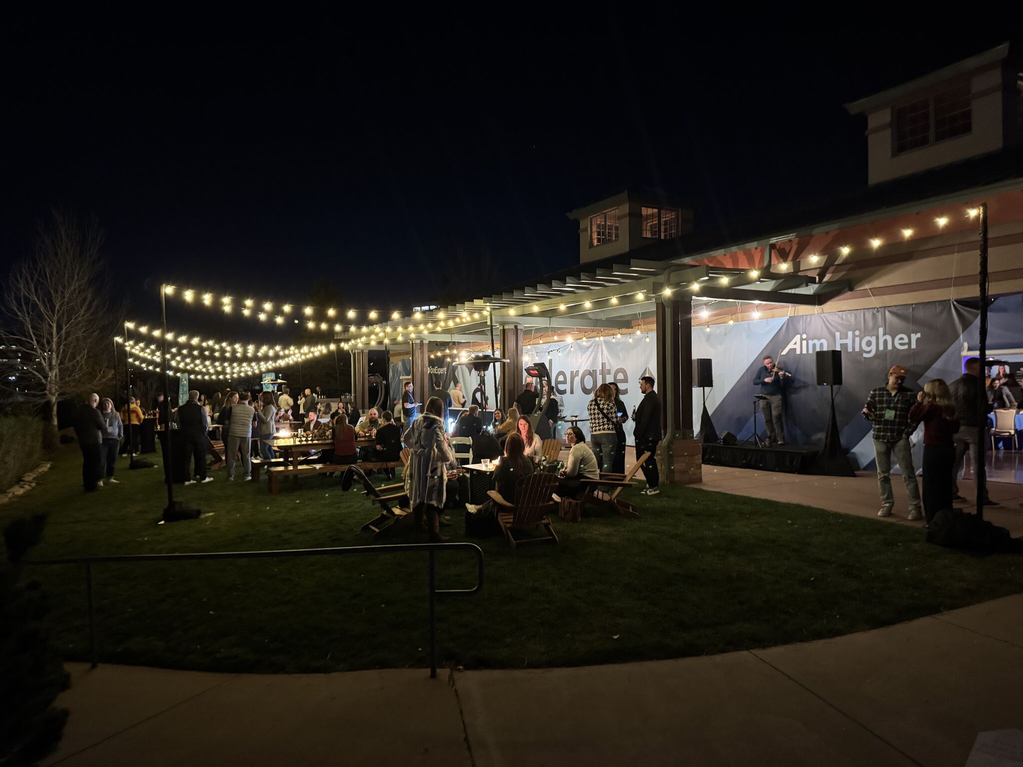 A festive outdoor party at night with fun lights and people networking.