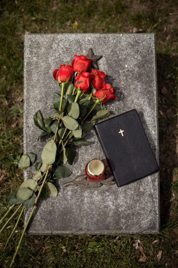 Nagrobek z czerwonymi różami, czarną Biblią ze złotym krzyżem i zniczem.