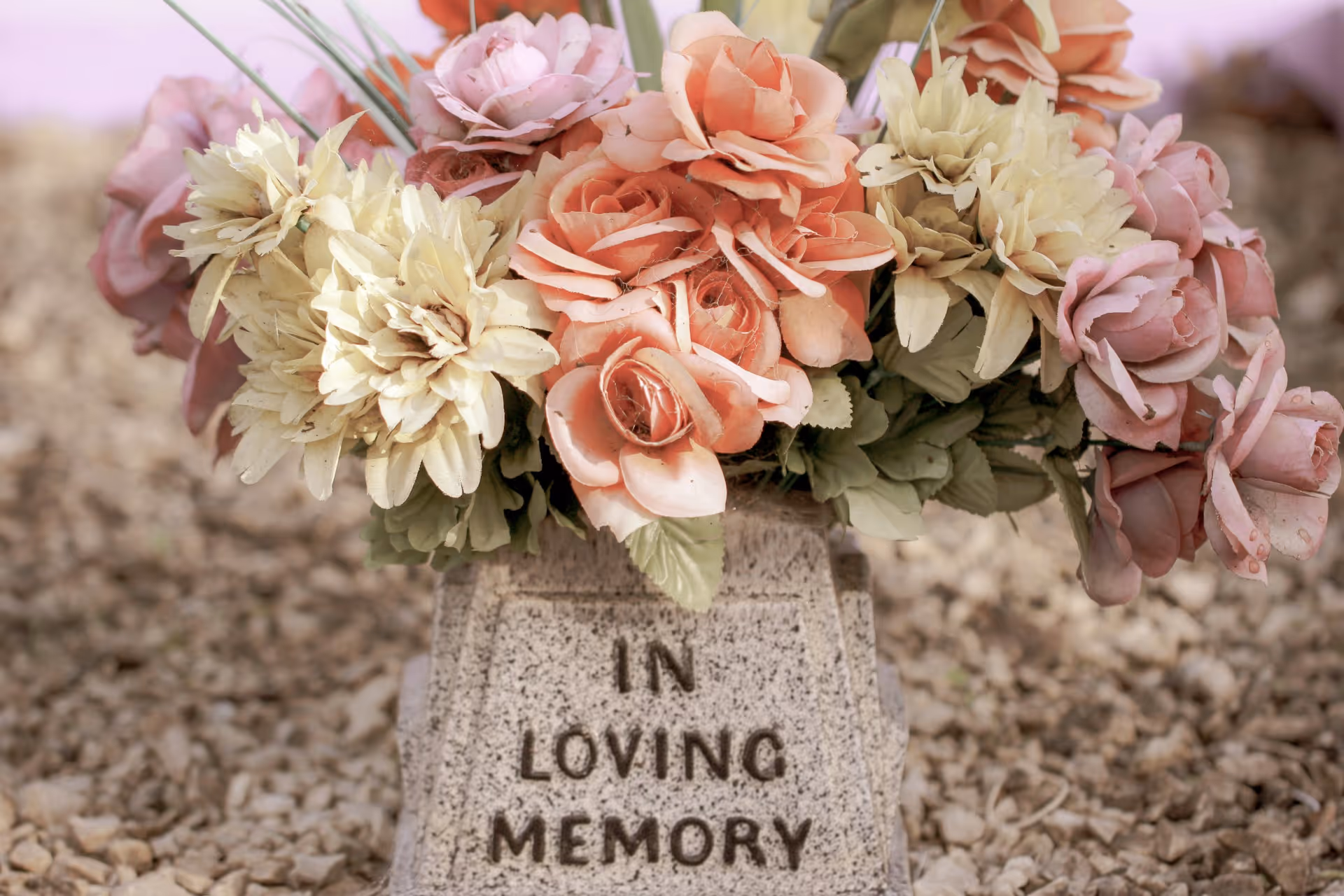 Bukiet pastelowych kwiatów położony na nagrobku z napisem „In Loving Memory”.