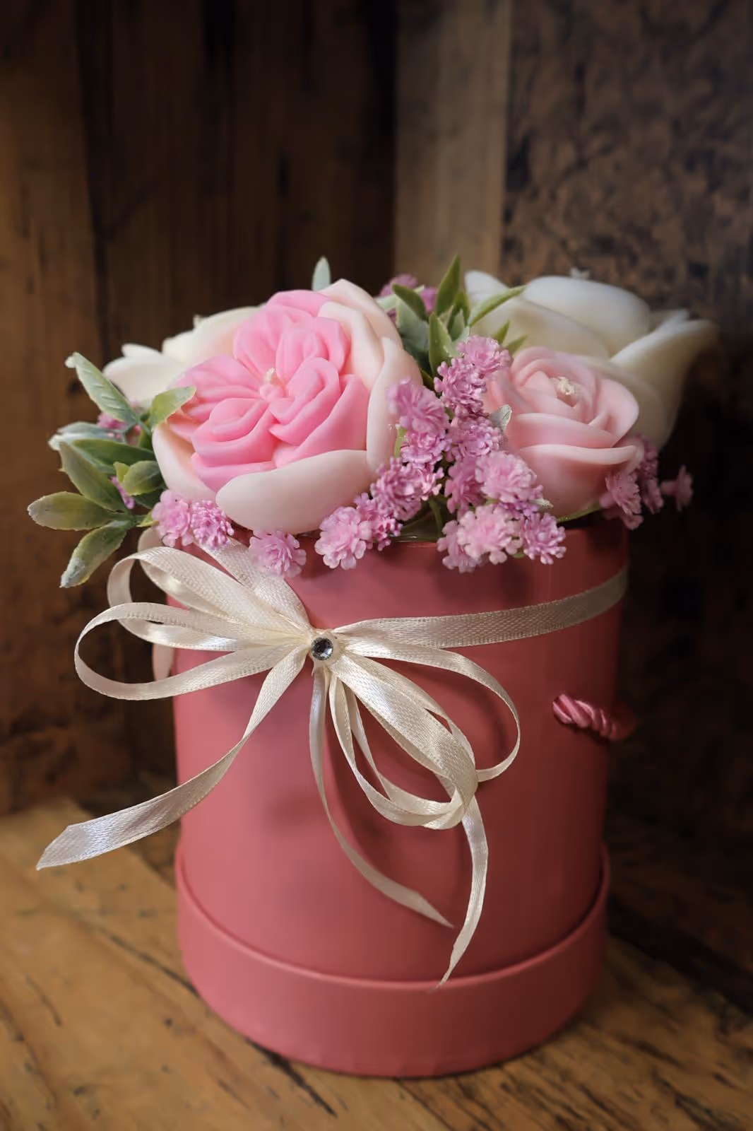 Dekoracyjna świeca w kształcie róż w czerwonym pudełku prezentowym z kokardką.