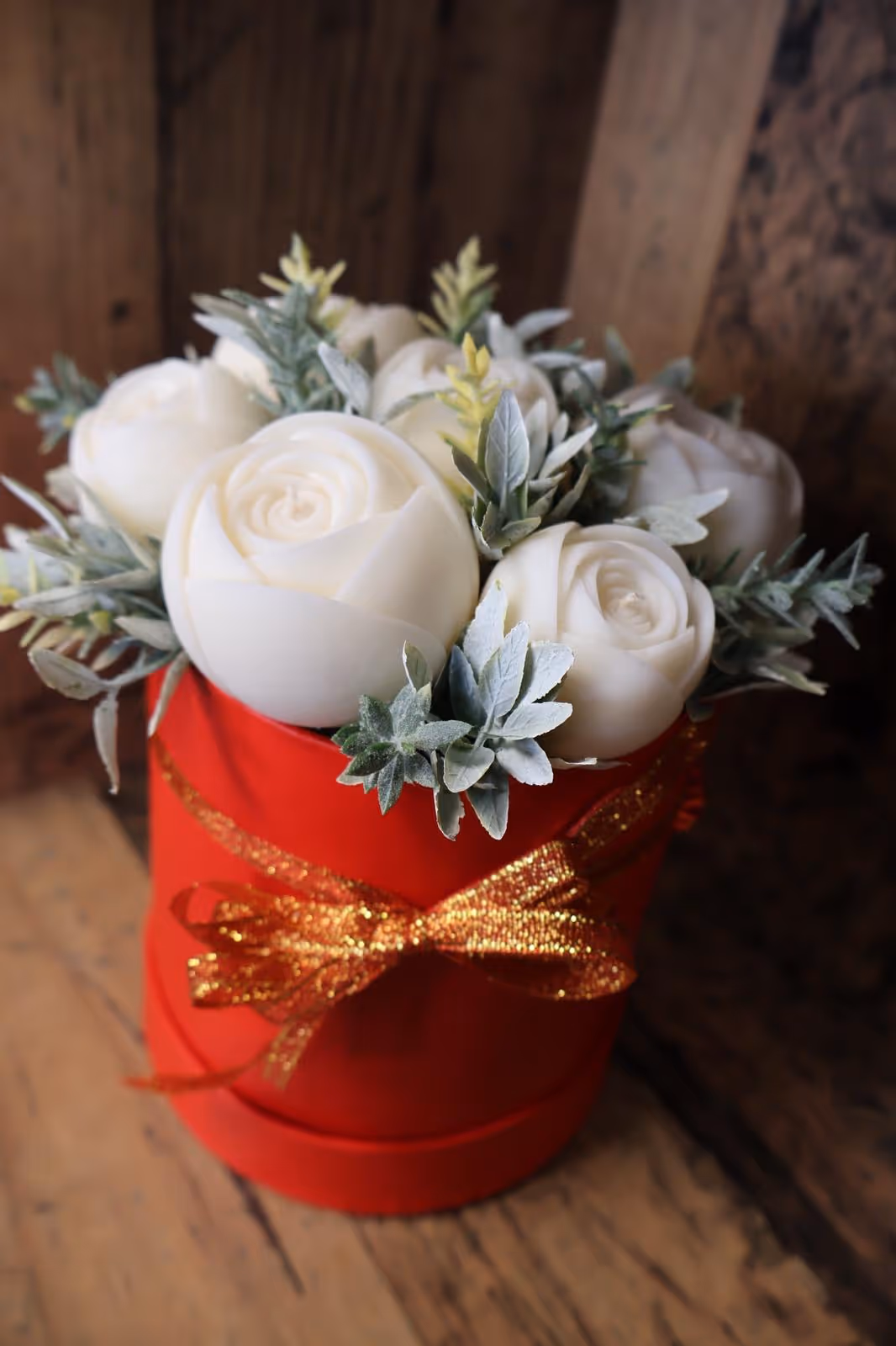 Dekoracyjna świeca w kształcie białych róż w czerwonym pudełku z zimowym akcentem.