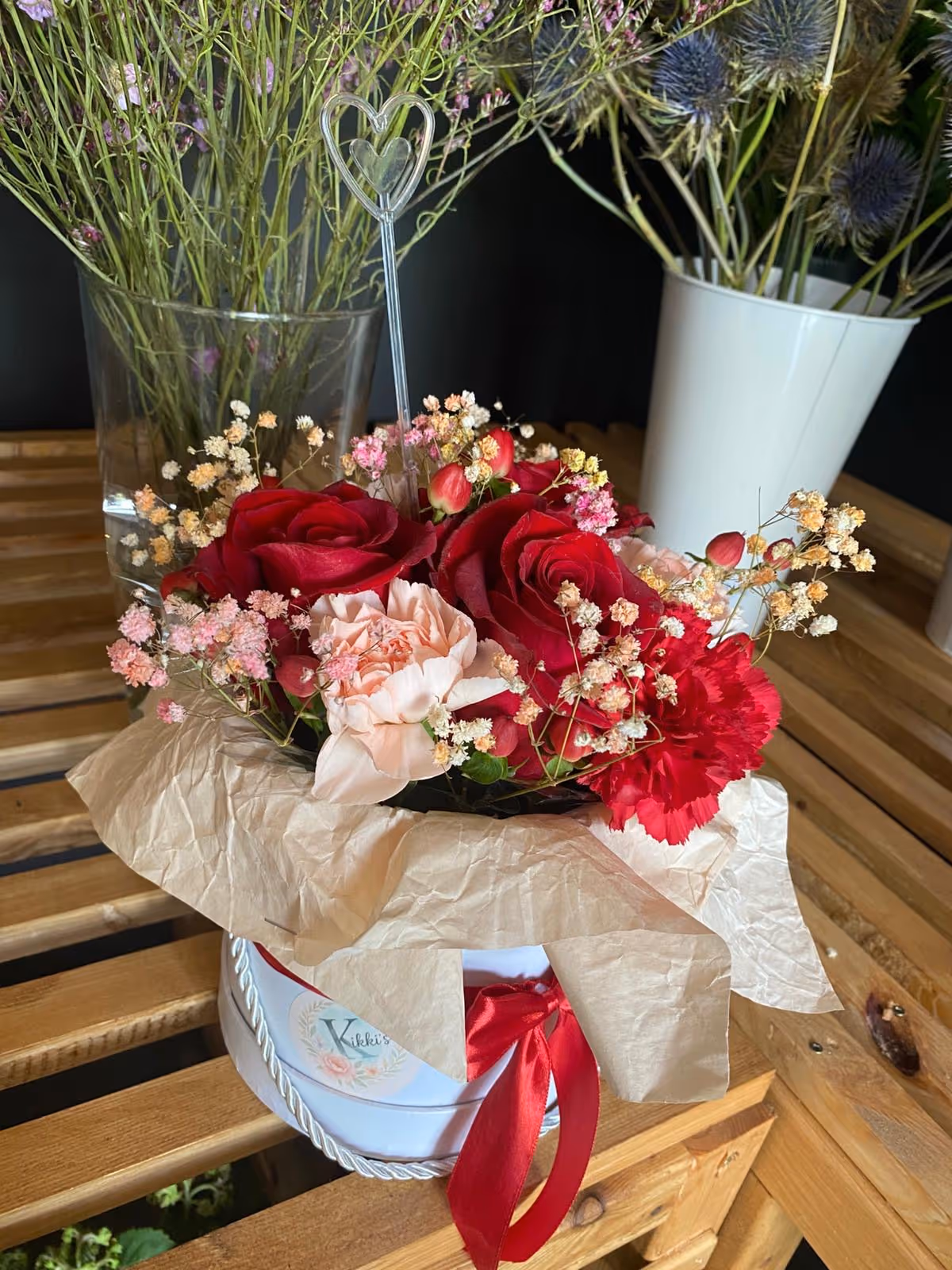 Romantyczny bukiet z czerwonymi różami, białymi goździkami i zielenią, owinięty w papier kraft.