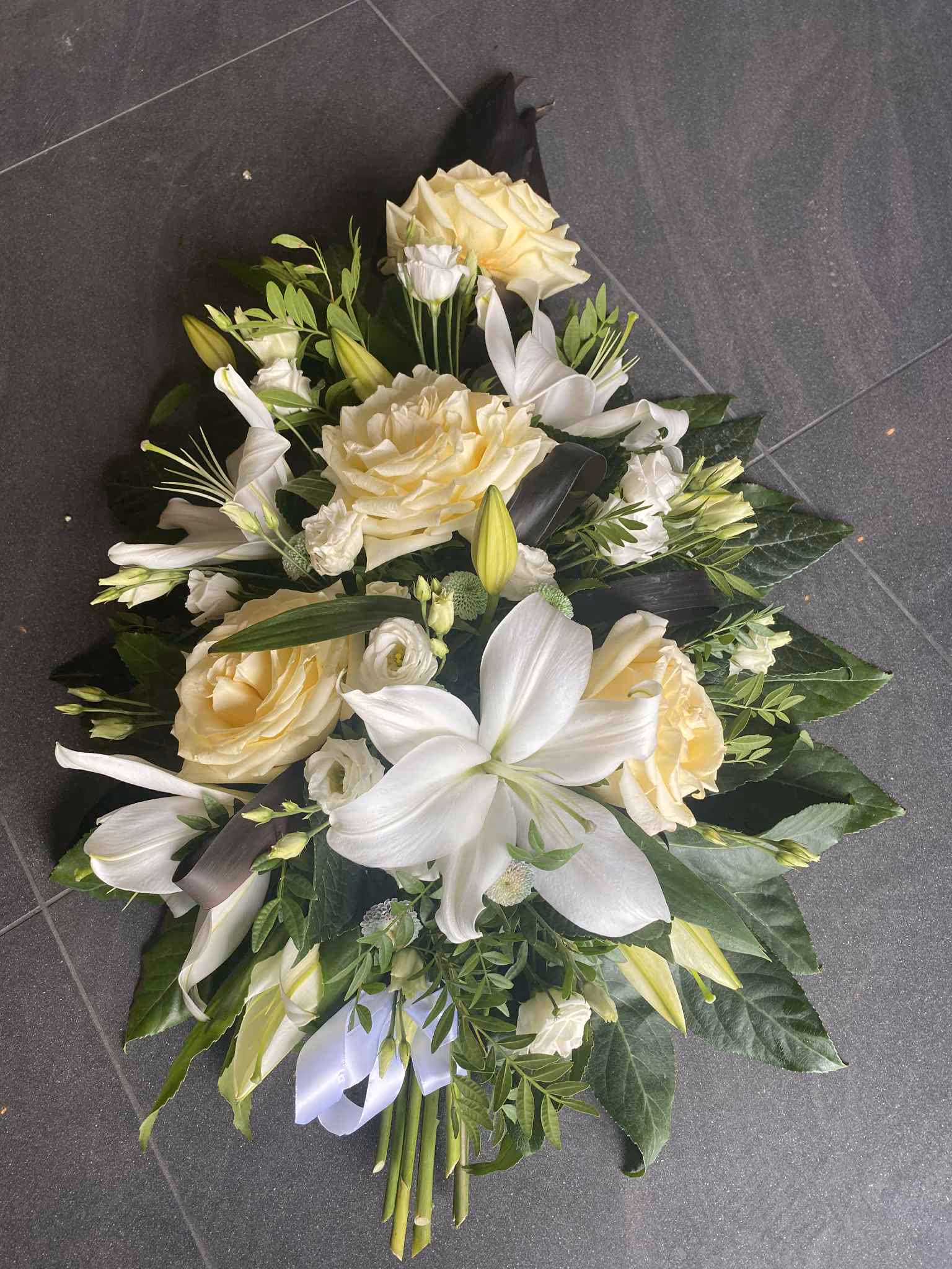Elegancka kompozycja z białymi liliami i kremowymi różami – idealna na uroczyste lub pogrzebowe okazje.