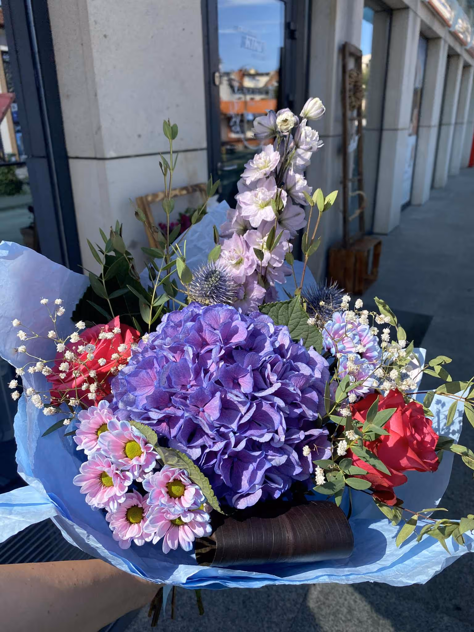 Kompozycja z intensywnie fioletową hortensją i margerytkami w ciemnym naczyniu.