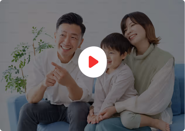 Smiling Asian family of three sitting on a blue couch, with the father pointing forward.
