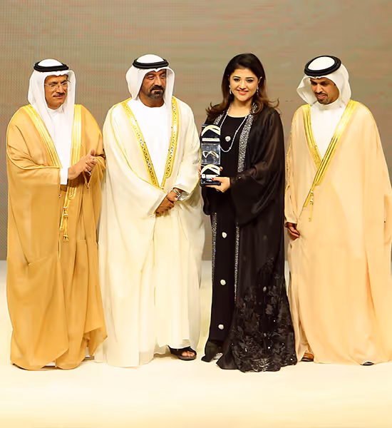 Four people in traditional Middle Eastern attire standing, with a woman holding an award trophy.