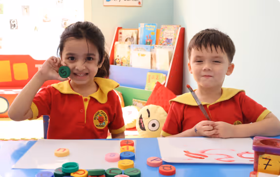 Woman in red shirt sitting at a table with a young girl, playing with colorful educational toys and abacus in a classroom.