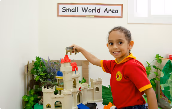 A woman in a red polo shirt and a young girl in a red and yellow shirt sitting at a table with colorful educational toys and games in a classroom.