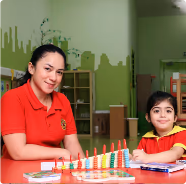 Teacher and young girl sitting at a table with colorful educational toys and books in a classroom.