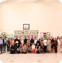 Large group of diverse women and children posing together indoors with framed pictures on the wall behind them.